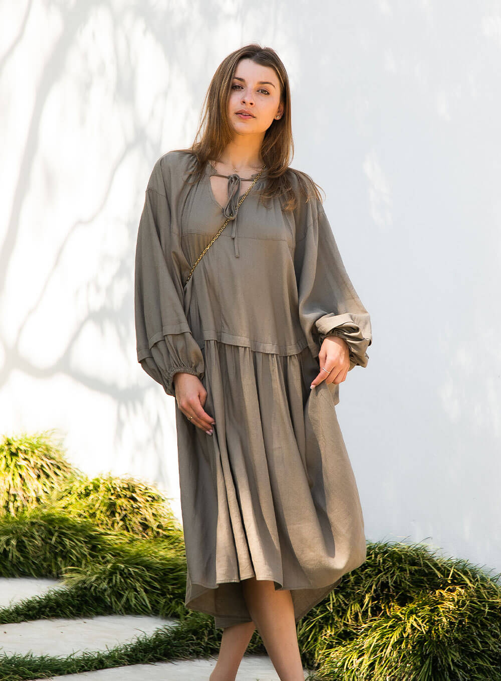 female model wearing Ada Line Dress-khaki midi dress with knee high boots on clear backdrop with floorboards