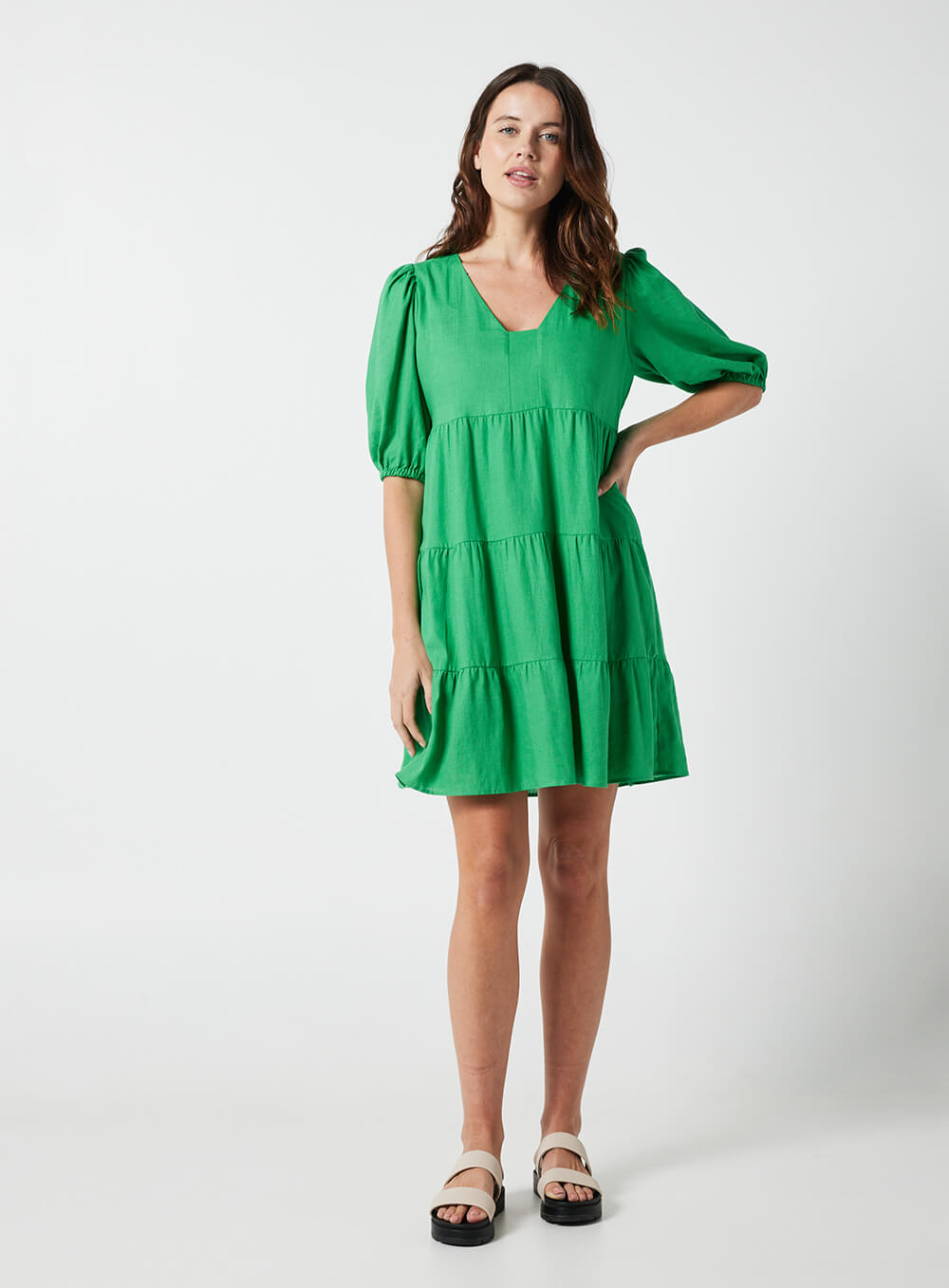 The Eleanor mini dress in green features a flowing layered a line shape with draping linen/viscose fabric, puff 3/4 sleeves with elastic cuff which can be pushed up to the elbow, a dropped v shape neckline with a square finish.
