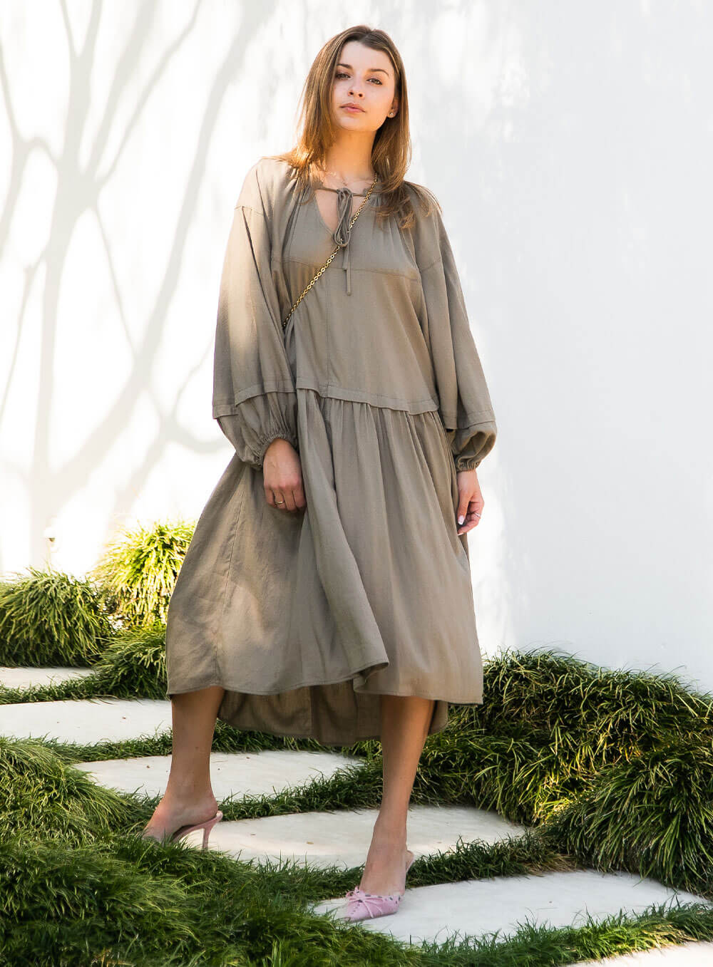 female model wearing Ada Line Dress-khaki midi dress with knee high boots on clear backdrop with floorboards