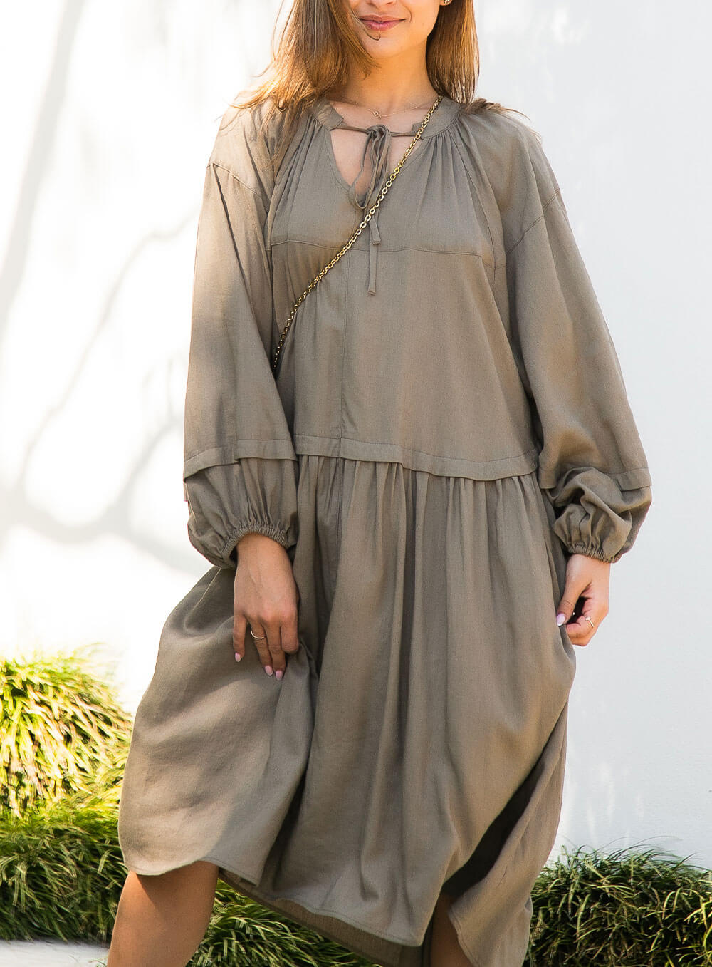 female model wearing Ada Line Dress-khaki midi dress with knee high boots on clear backdrop with floorboards