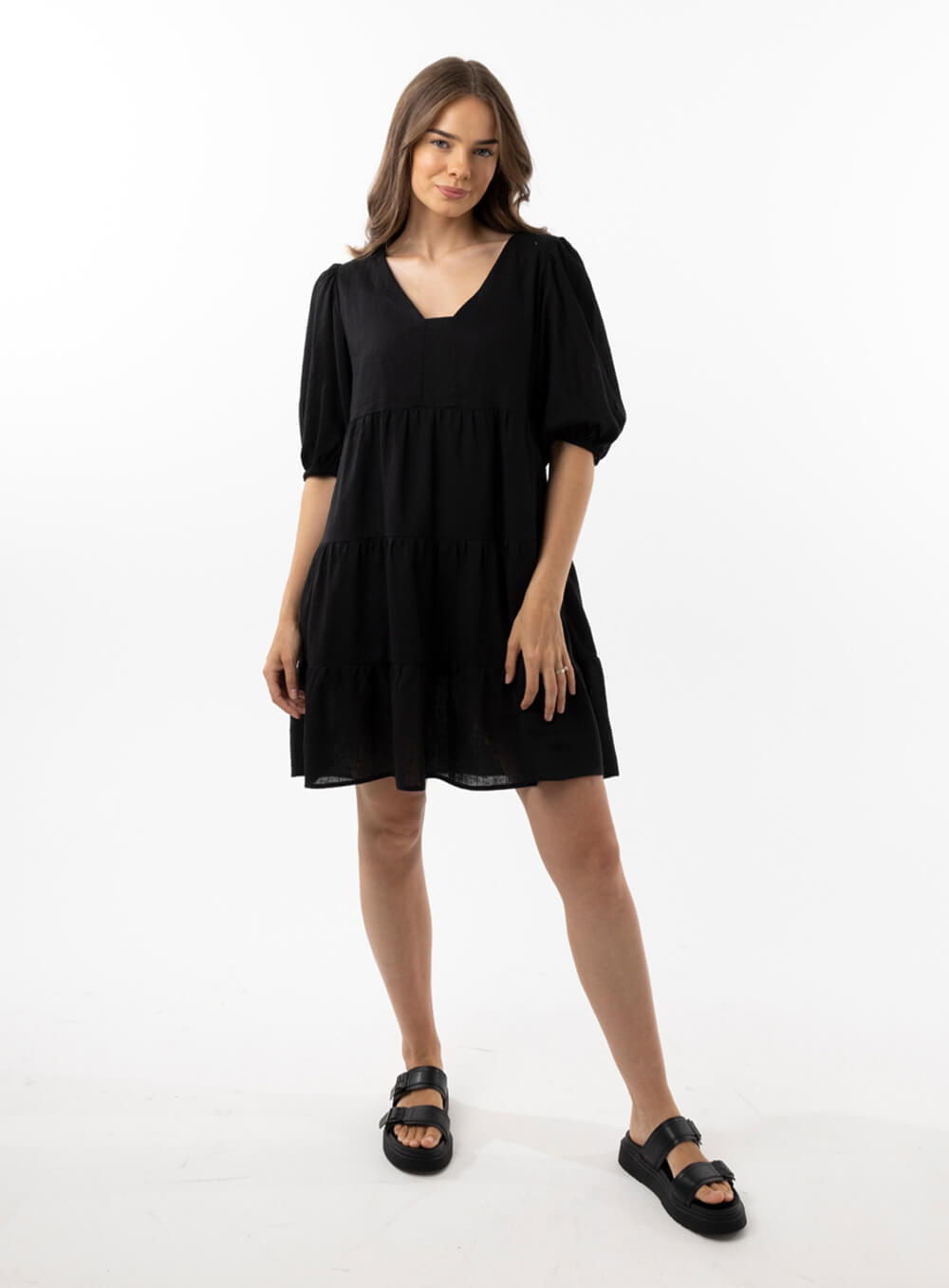 The Eleanor mini dress in black features a flowing layered a line shape with draping linen/viscose fabric, puff 3/4 sleeves with elastic cuff which can be pushed up to the elbow, a dropped v shape neckline with a square finish.