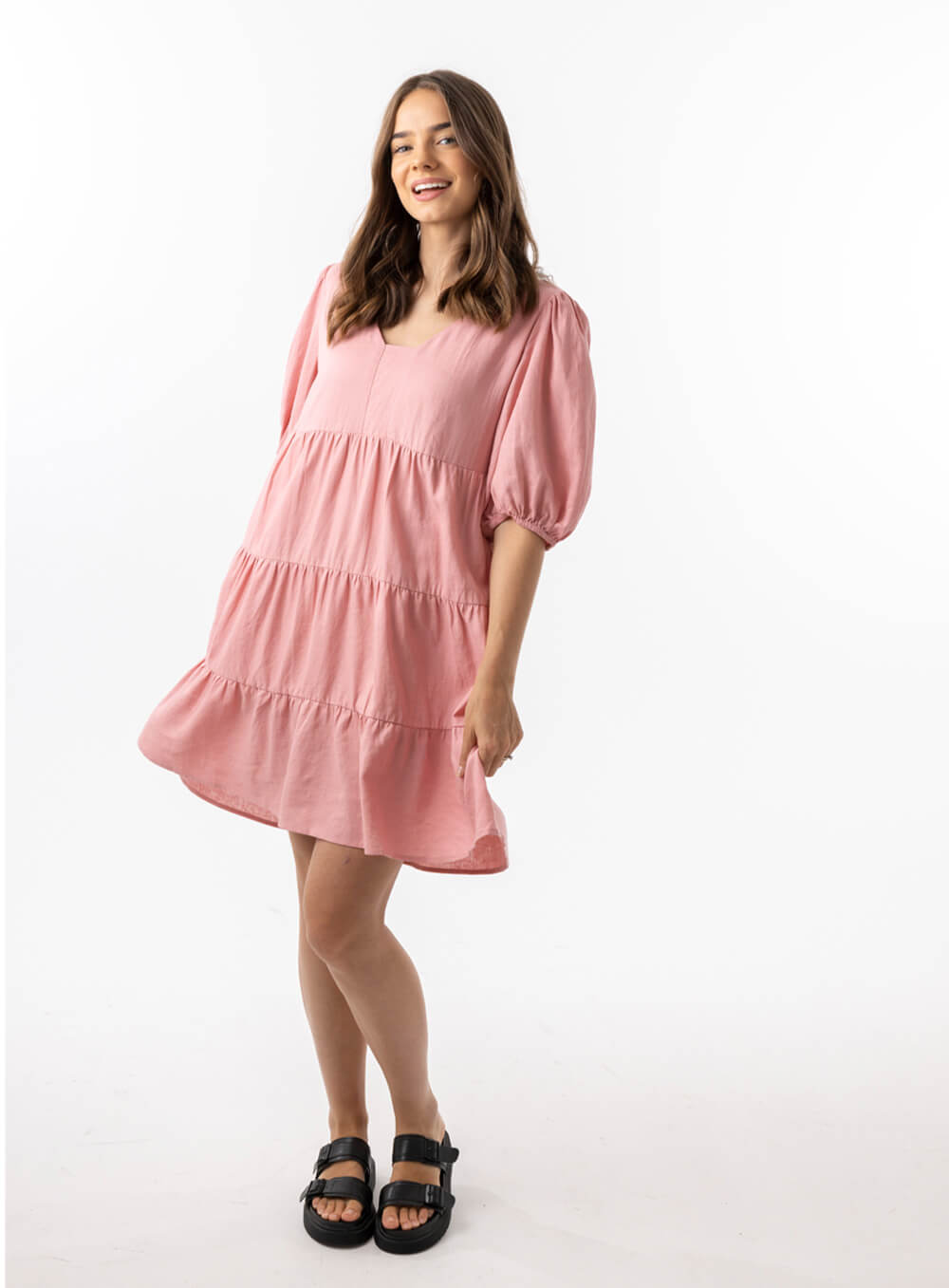 The Eleanor mini dress in blush pink features a flowing layered a line shape with draping linen/viscose fabric, puff 3/4 sleeves with elastic cuff which can be pushed up to the elbow, a dropped v shape neckline with a square finish.