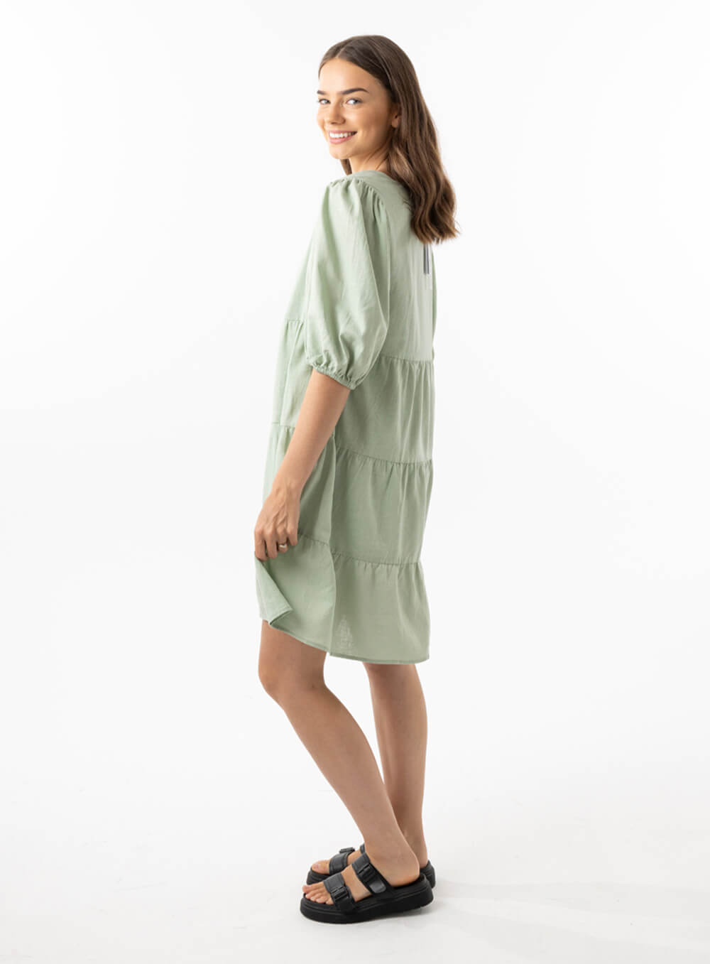 The Eleanor mini dress in sage features a flowing layered a line shape with draping linen/viscose fabric, puff 3/4 sleeves with elastic cuff which can be pushed up to the elbow, a dropped v shape neckline with a square finish.