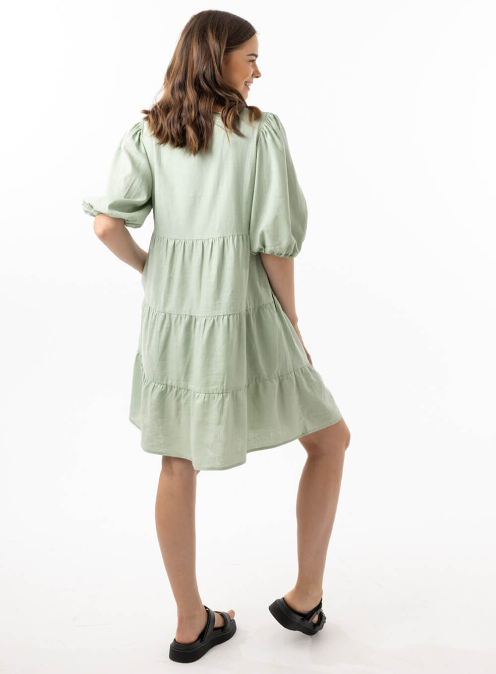 The Eleanor mini dress in sage features a flowing layered a line shape with draping linen/viscose fabric, puff 3/4 sleeves with elastic cuff which can be pushed up to the elbow, a dropped v shape neckline with a square finish.