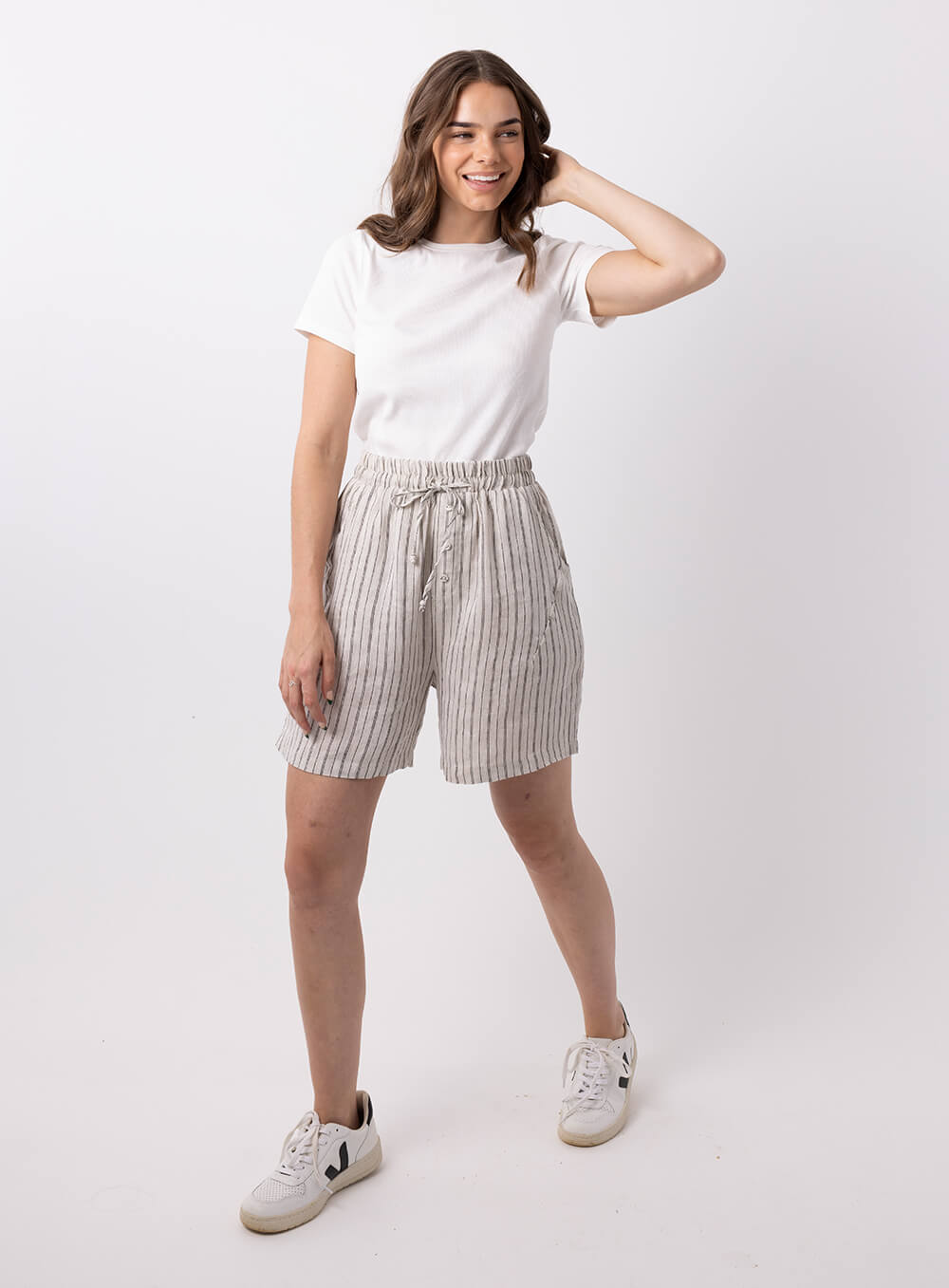 The Evan stripe linen shorts in beige colour with black thin stripes is made in 100% linen, features 2 side pockets and 2 back pockets, has wide elastic waistband with tie, 3 mock buttons and finish mid thigh length.