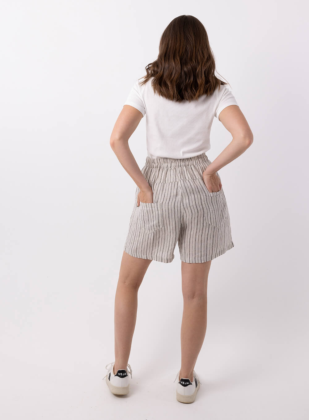 The Evan stripe linen shorts in beige colour with black thin stripes is made in 100% linen, features 2 side pockets and 2 back pockets, has wide elastic waistband with tie, 3 mock buttons and finish mid thigh length.