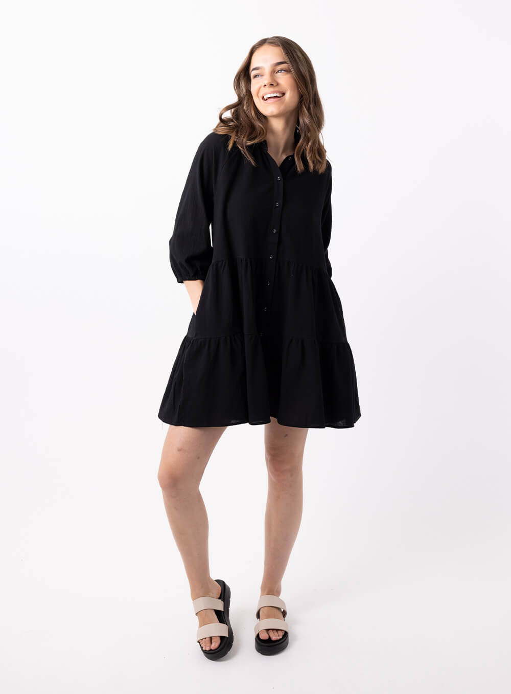 The Jasmine Dress in black is made of 100% soft cotton, featuring a collar neck, 3/4 sleeve with elastic cuff button through front all the way to the hem, tiered layers through the body, midi in length and 2 side pockets
