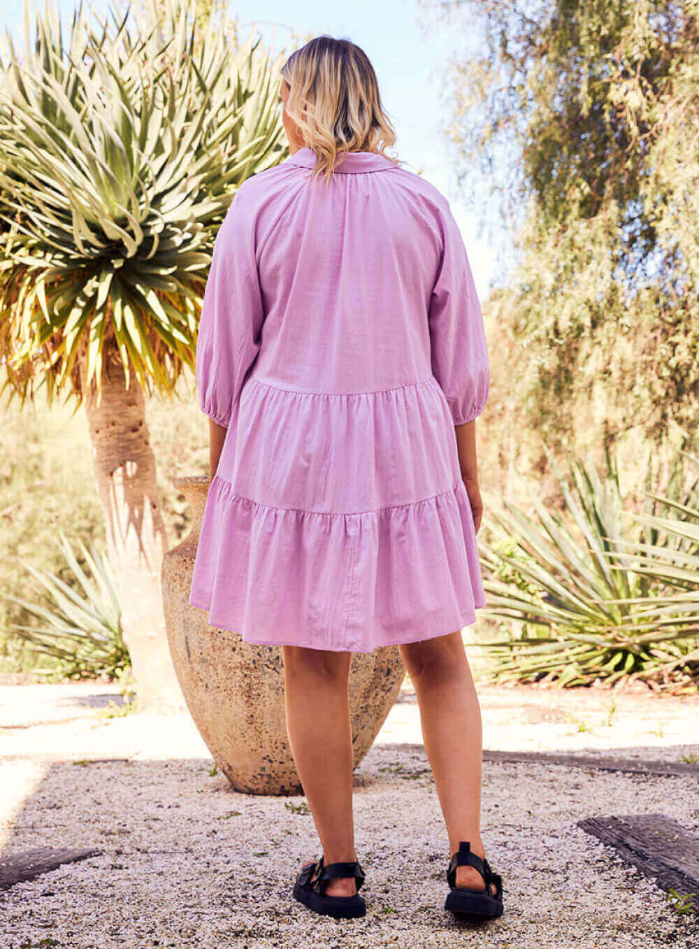 The Jasmine Dress in lilac is made of 100% soft cotton, featuring a collar neck, 3/4 sleeve with elastic cuff button through front all the way to the hem, tiered layers through the body, midi in length and 2 side pockets