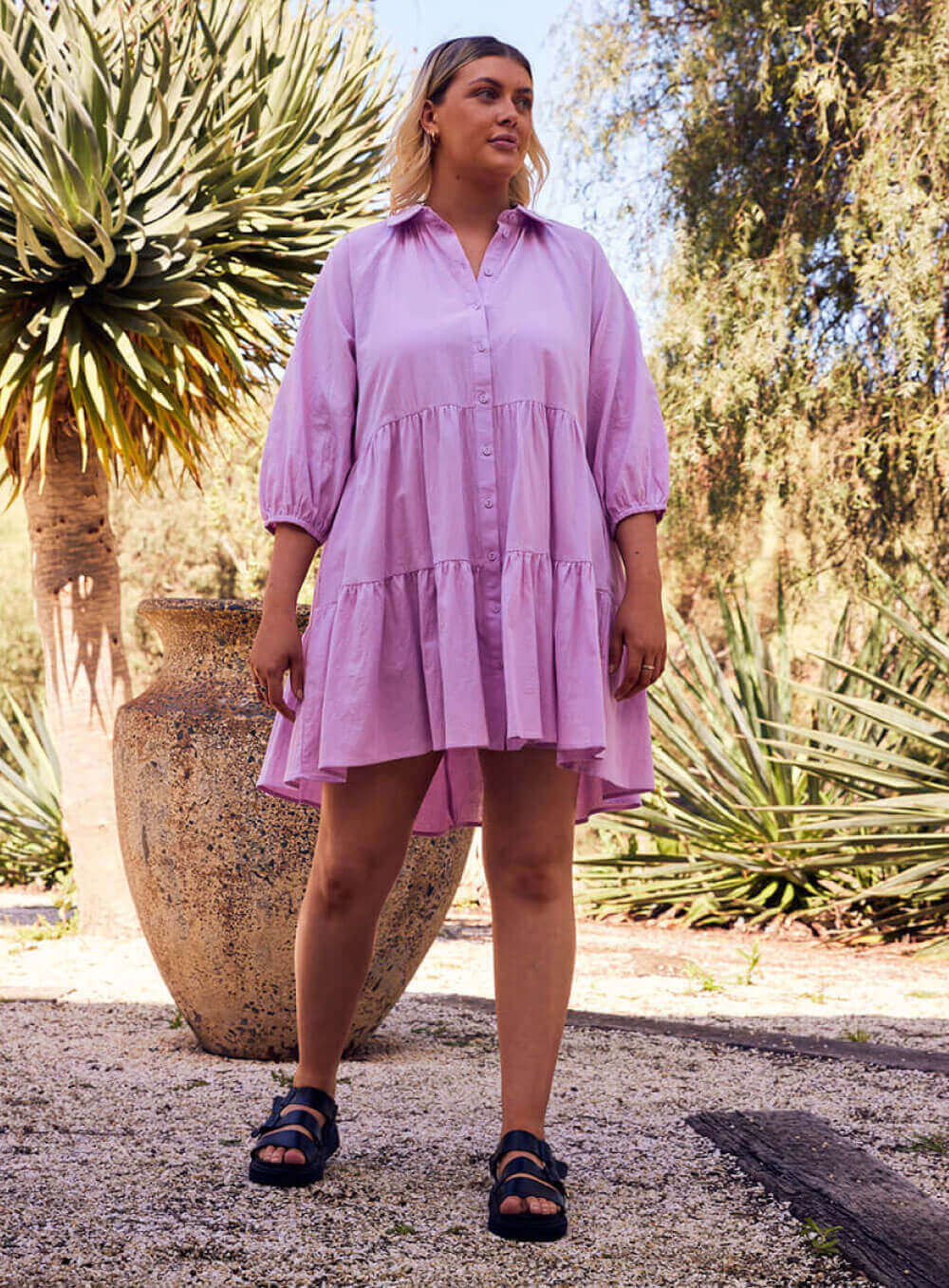 The Jasmine Dress in lilac is made of 100% soft cotton, featuring a collar neck, 3/4 sleeve with elastic cuff button through front all the way to the hem, tiered layers through the body, midi in length and 2 side pockets