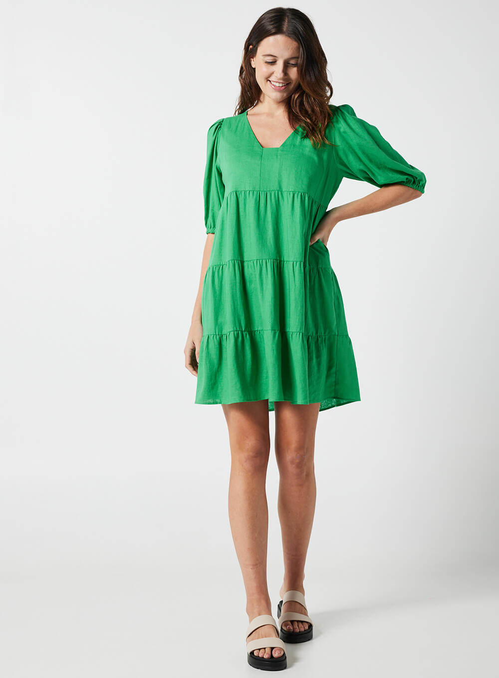 The Eleanor mini dress in green features a flowing layered a line shape with draping linen/viscose fabric, puff 3/4 sleeves with elastic cuff which can be pushed up to the elbow, a dropped v shape neckline with a square finish.